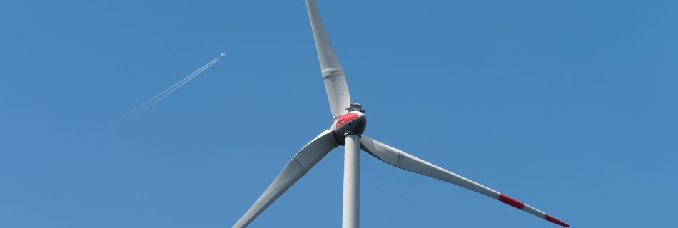 A wind turbine in the foreground with a jet flying high above.