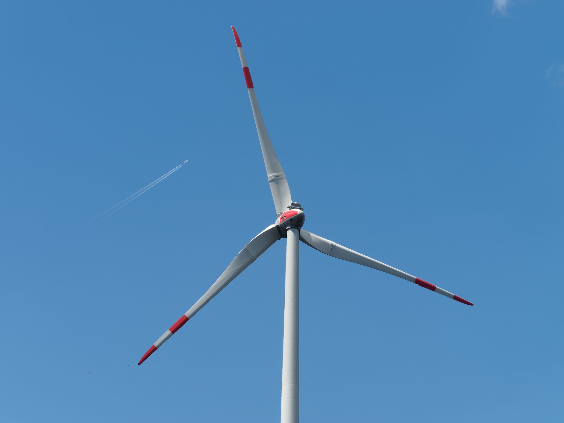 A wind turbine in the foreground with a jet flying high above.